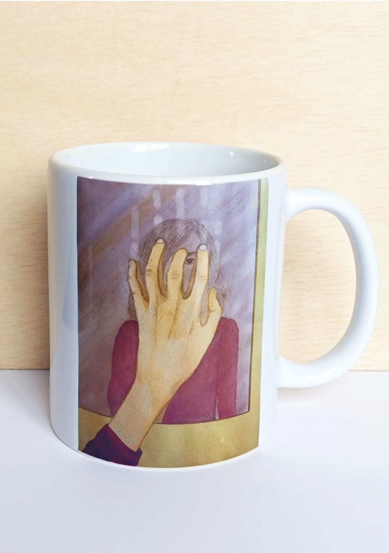 Taza de cerámica blanca por delante, con ilustración que representa a una persona mirándose al espejo y posando una mano sobre él.