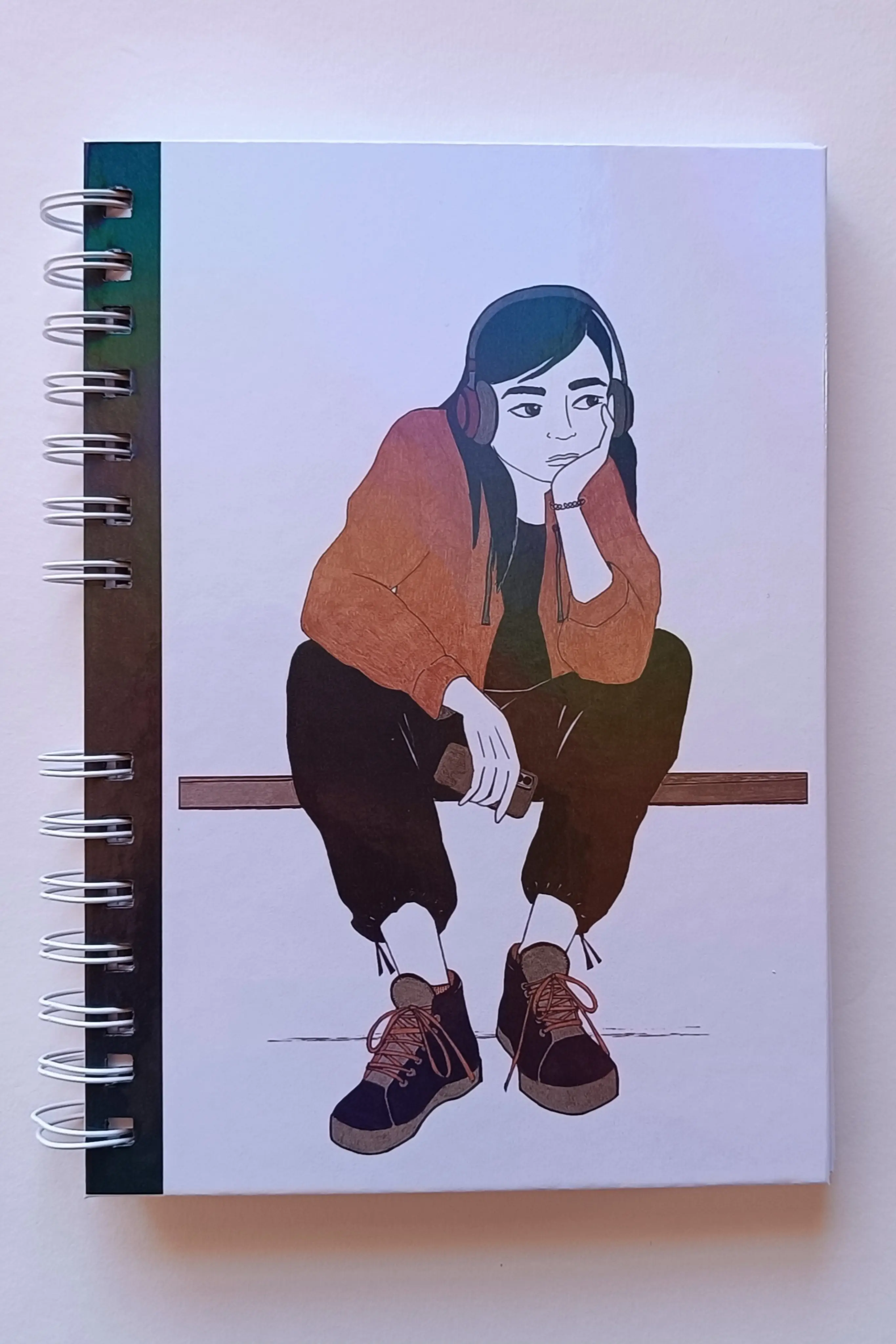 Portada de libreta tamaño A5, con fondo blanco e ilustración que representa una chica sentada con auriculares.