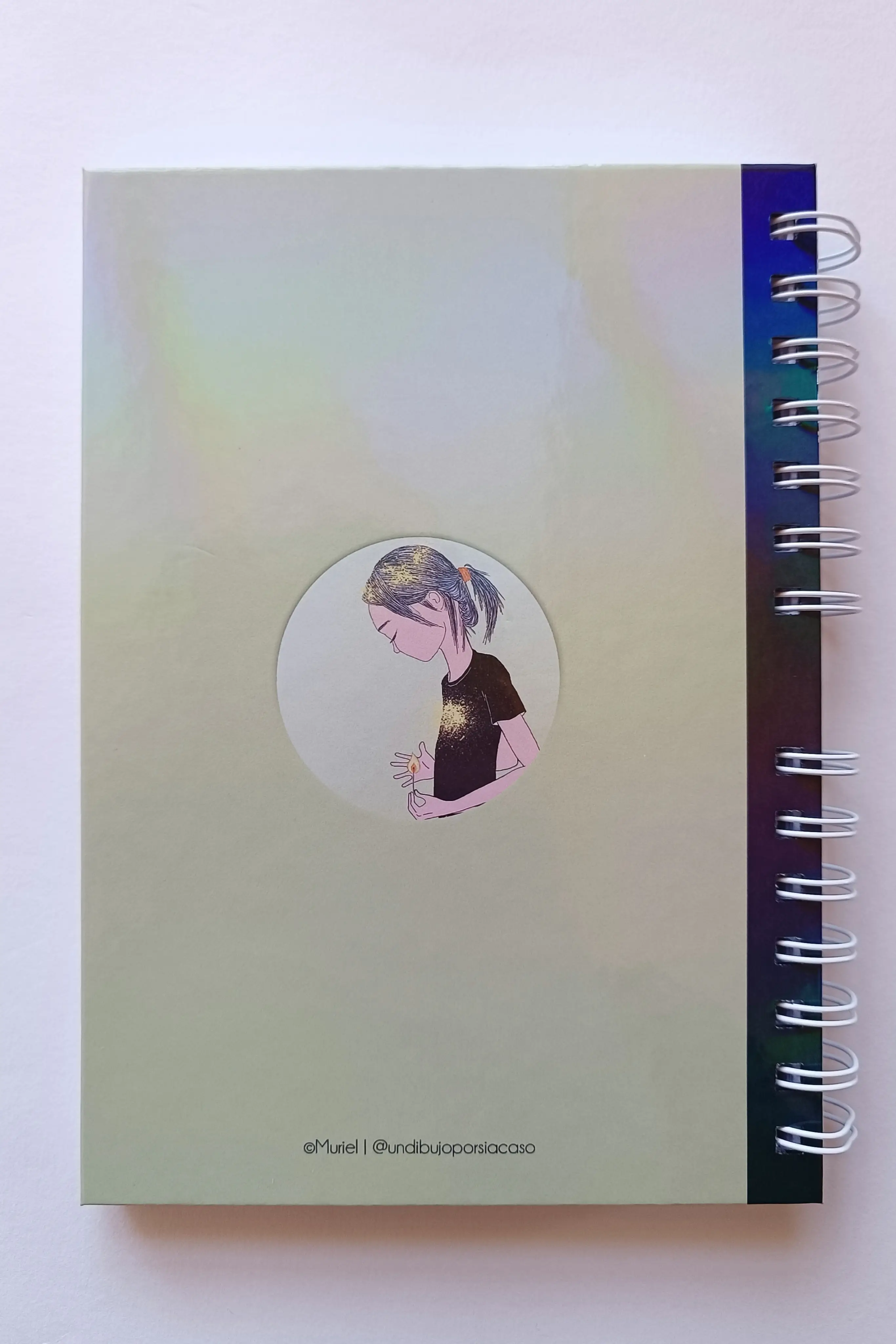 Contraportada de libreta tamaño A5, con fondo verde claro e ilustración pequeña y centrada que representa a una niña de perfil con una cerilla en la mano dentro de un círculo.