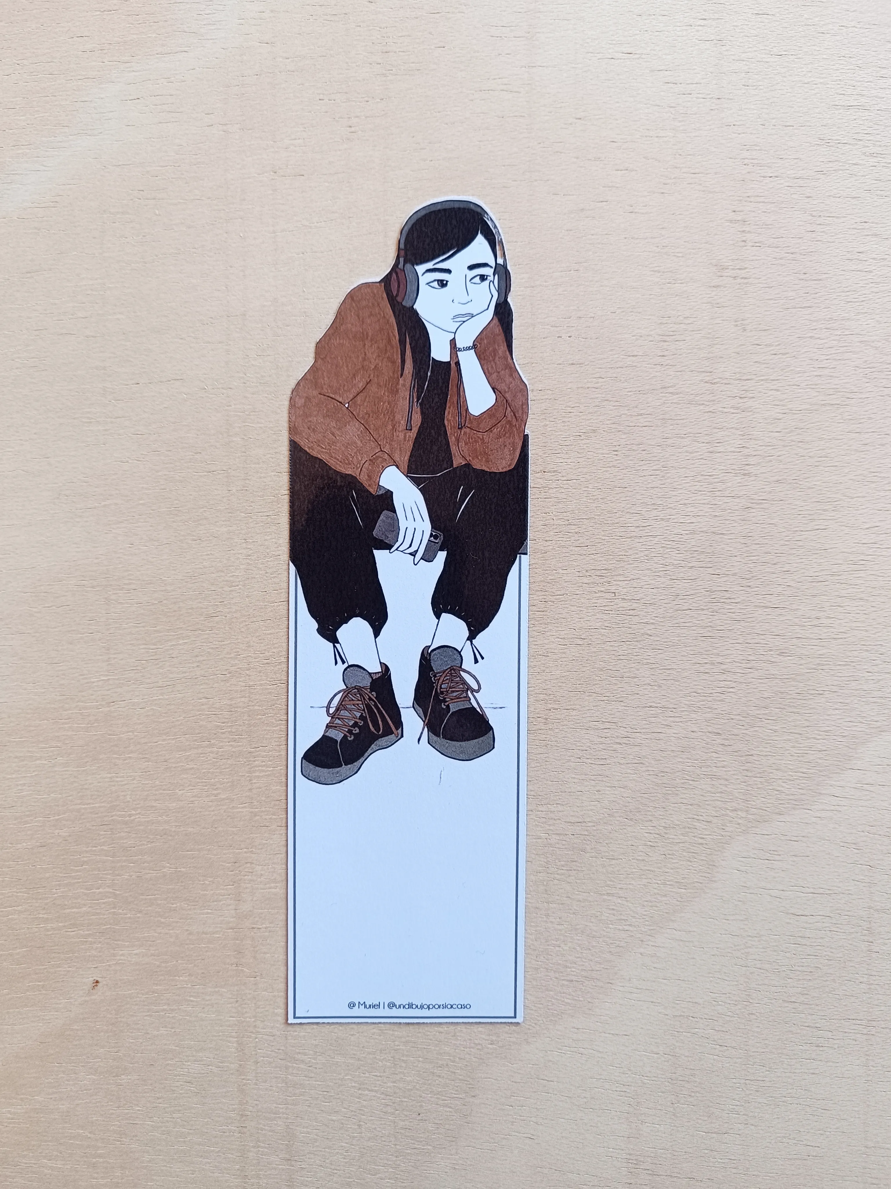 Marcapáginas con ilustración que representa una chica sentada con auriculares y móvil en la mano.